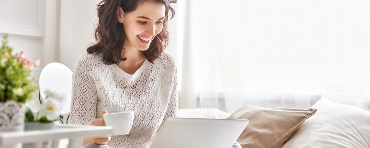 Woman drinking coffee and looking at her laptop
